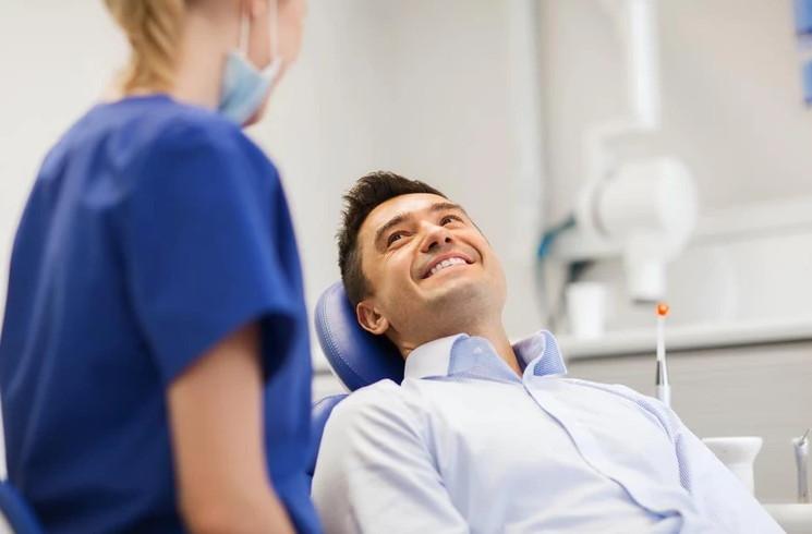 Uśmiechnięty mężczyzna na fotelu dentystycznym, patrzący na dentystkę z zadowoleniem.