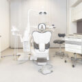 Białe wnętrze gabinetu dentystycznego. Na środku jest fotel dla pacjenta i sprzęt stomatologiczny. A po bokach białe szafki biurowe.